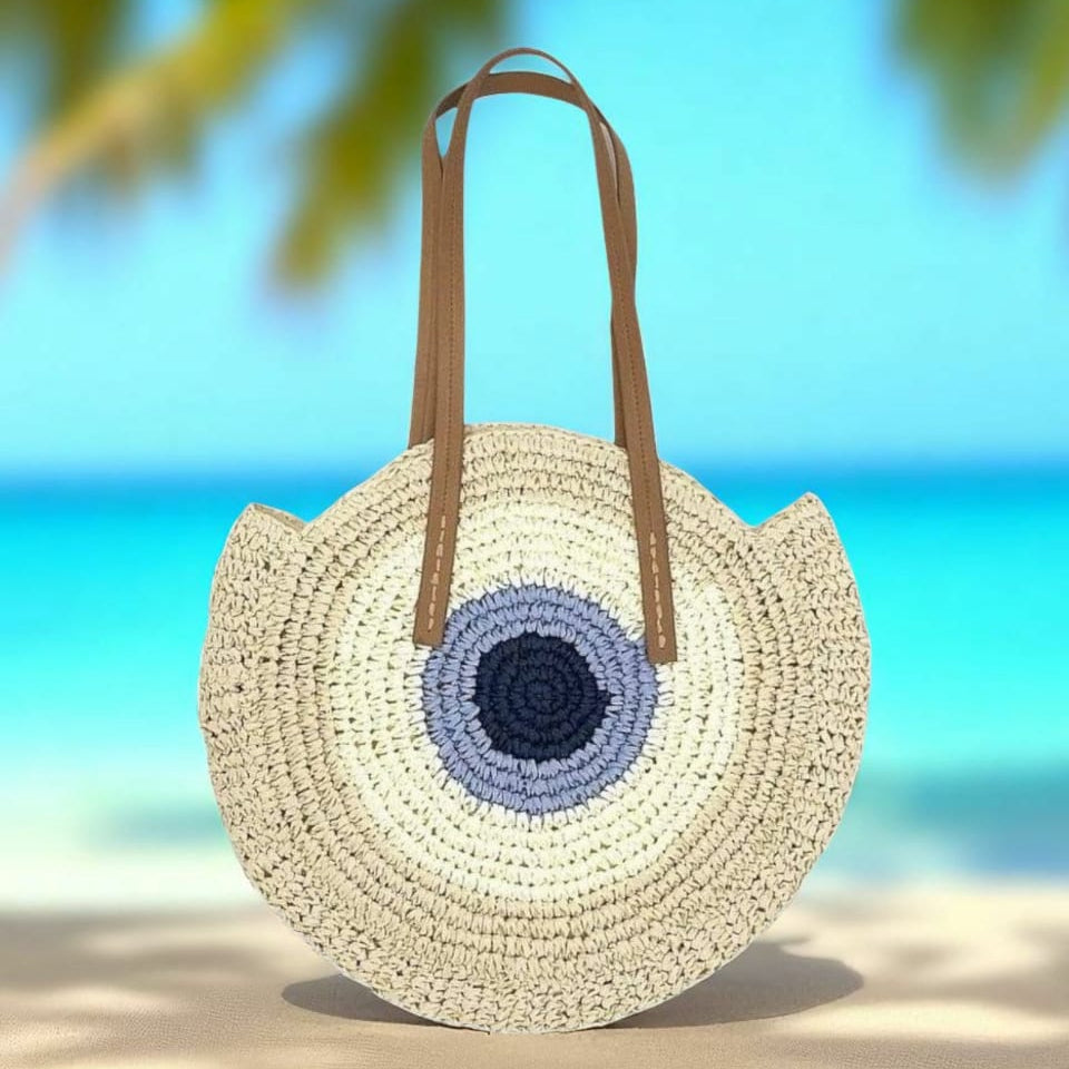 Round woven bag with a blue and purple center on a beach with palm leaves.