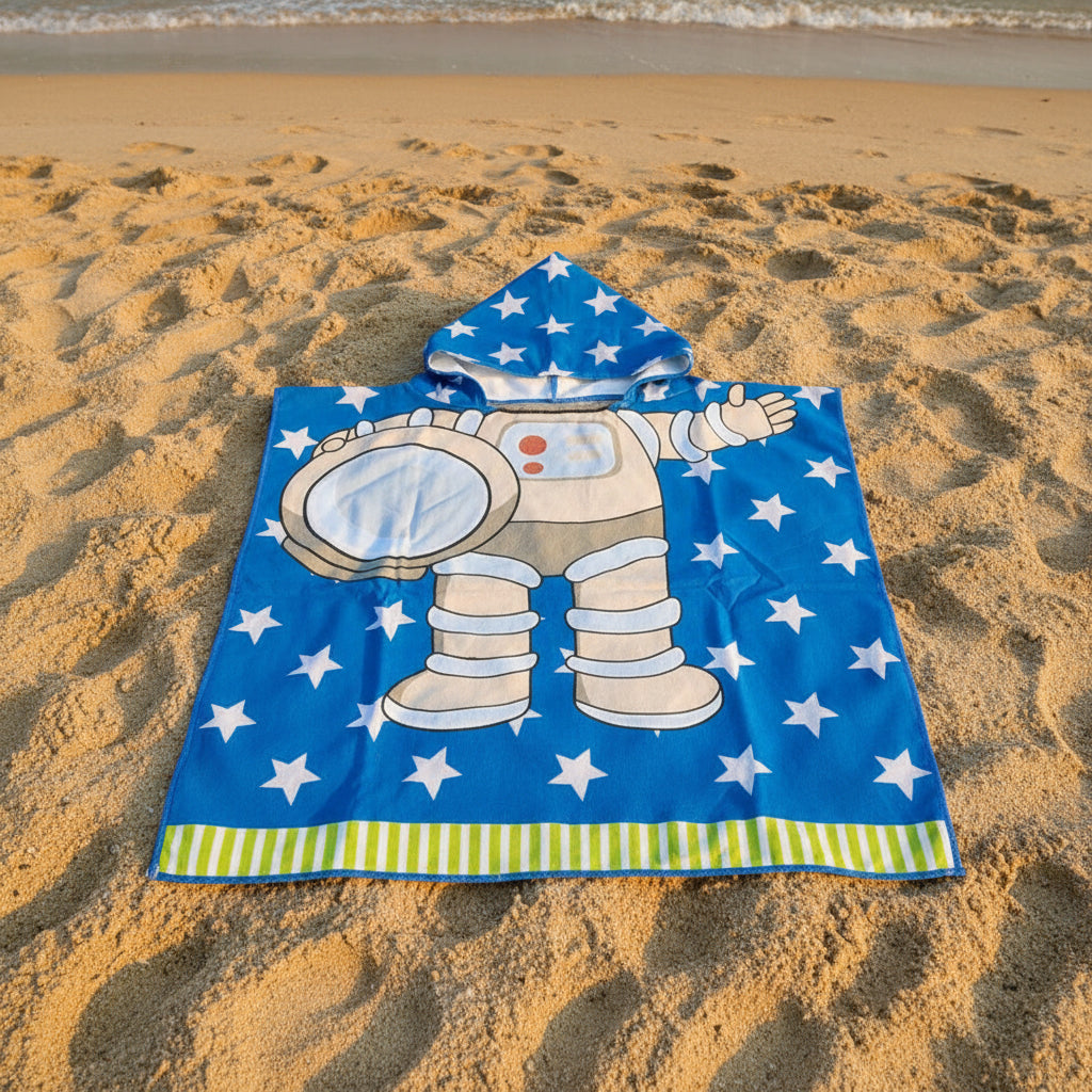 Blue astronaut poncho towel with a spacesuit print and green striped hem flat lay on sand