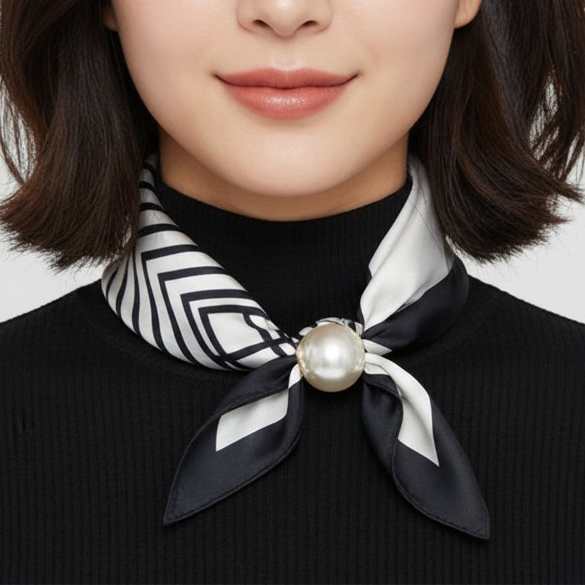 Person wearing a black and white patterned foulard with a pearl accent on a plain background