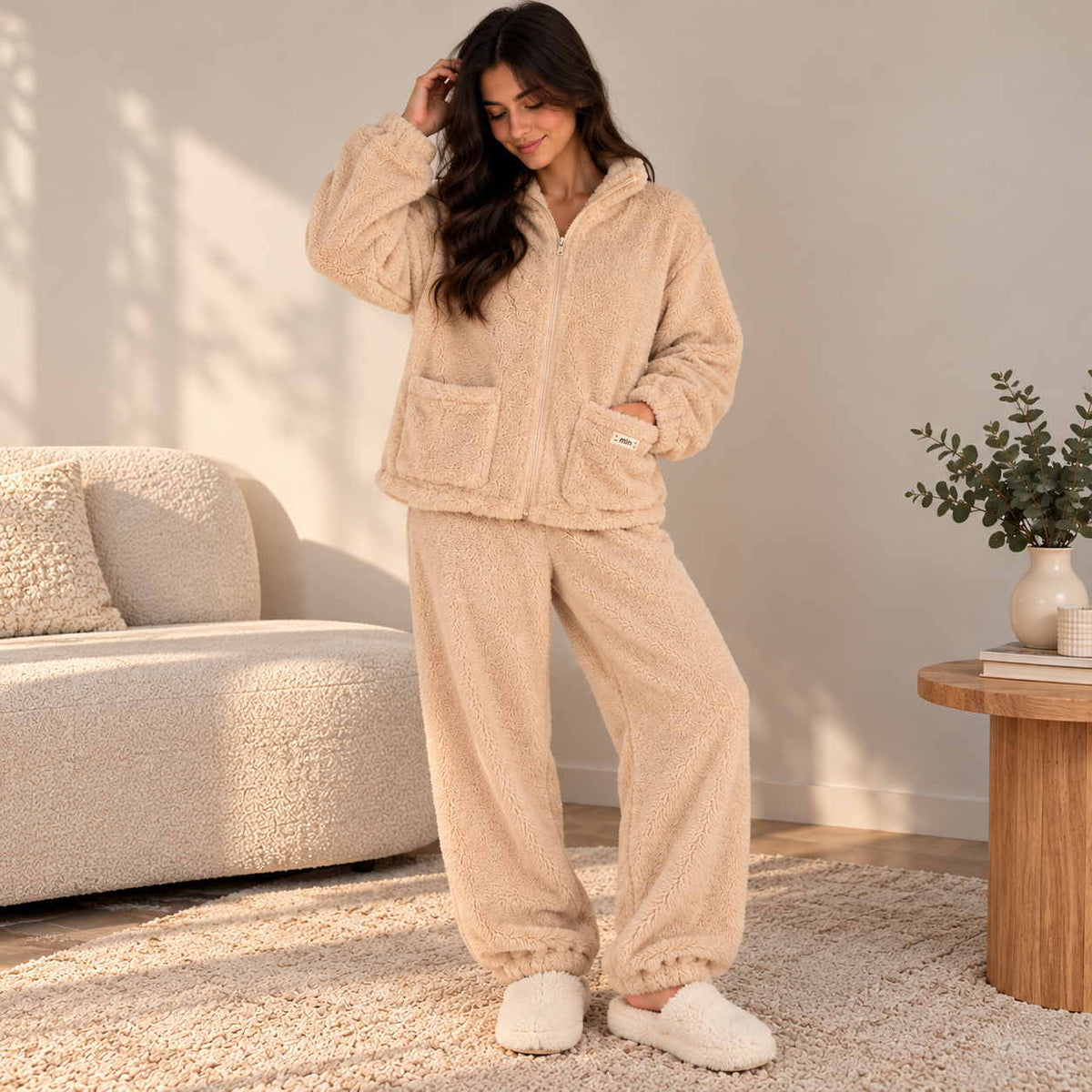 Woman in a beige teddy fleece zip jacket and cuffed jogger set with fluffy slippers at home
