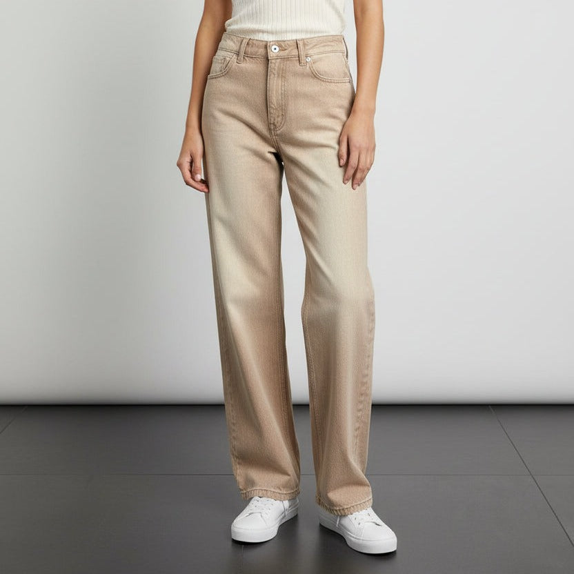 Person wearing beige wide jeans and white sneakers on a plain background