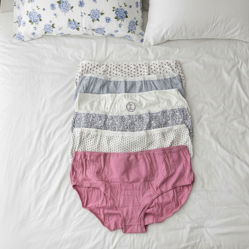 Full coverage briefs stacked on a white bed, a solid pink pair on top