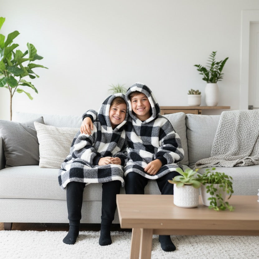 Two kids sitting together in buffalo check hooded blankets