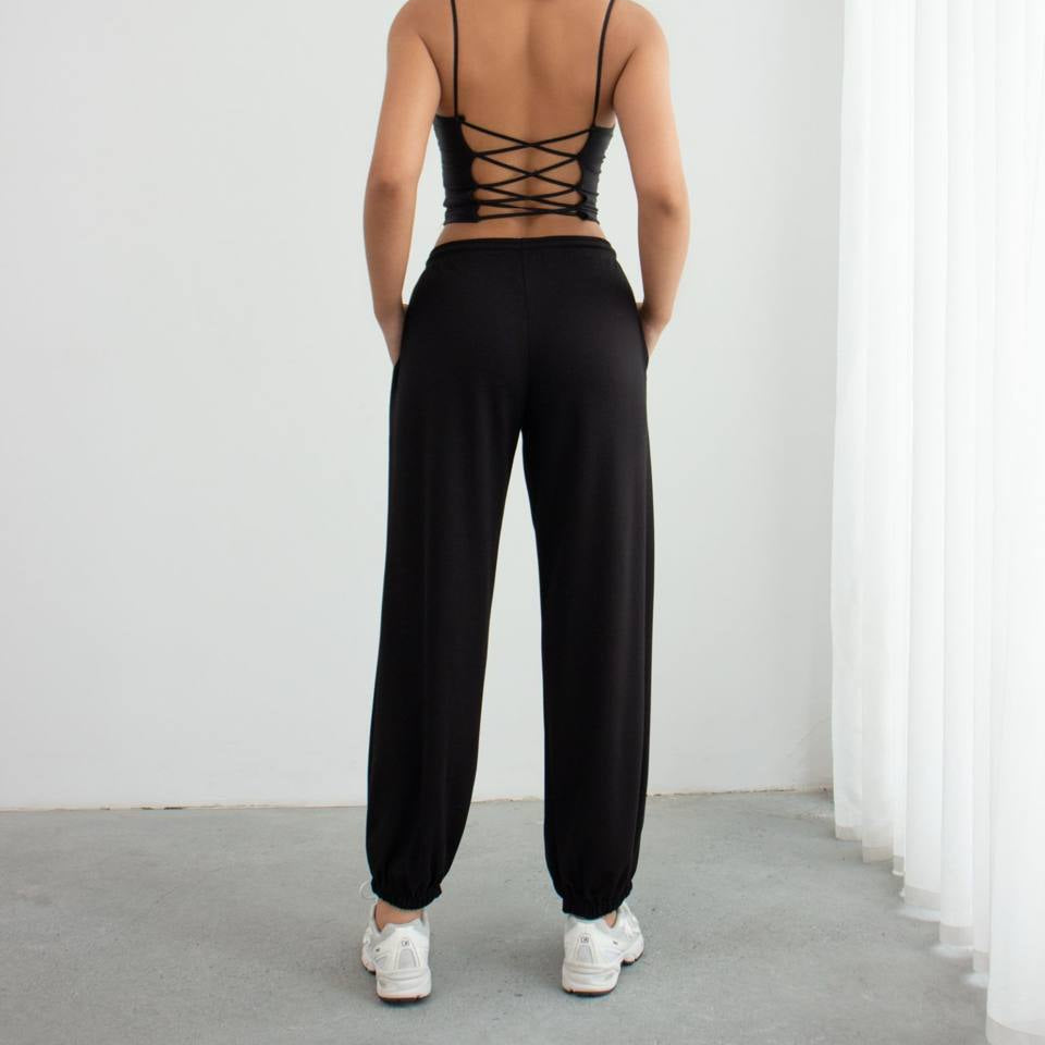 Person wearing a black strappy top and black pants against a white background
