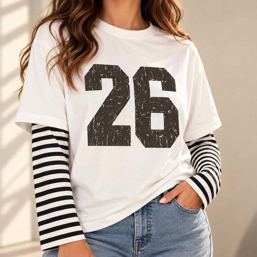 Woman in a white tee with a distressed black 26 print and black striped long sleeves