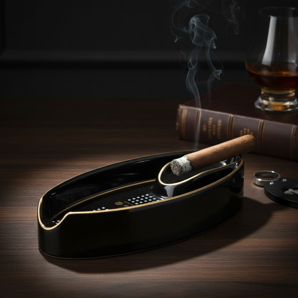 Lit cigar resting in a slim black oval ashtray beside a whiskey glass and books