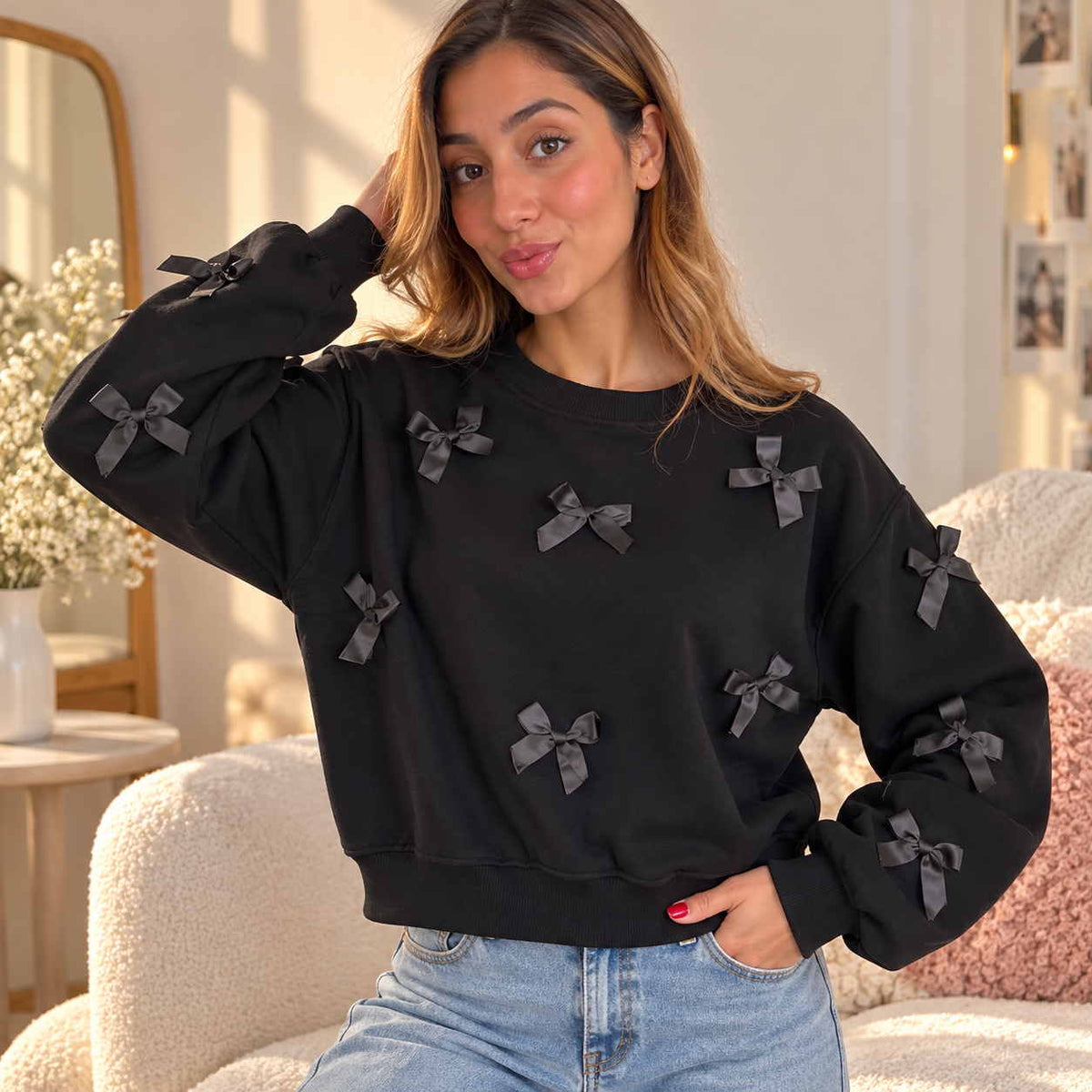 Woman in a black cropped sweatshirt covered in black satin bows, hand in her hair