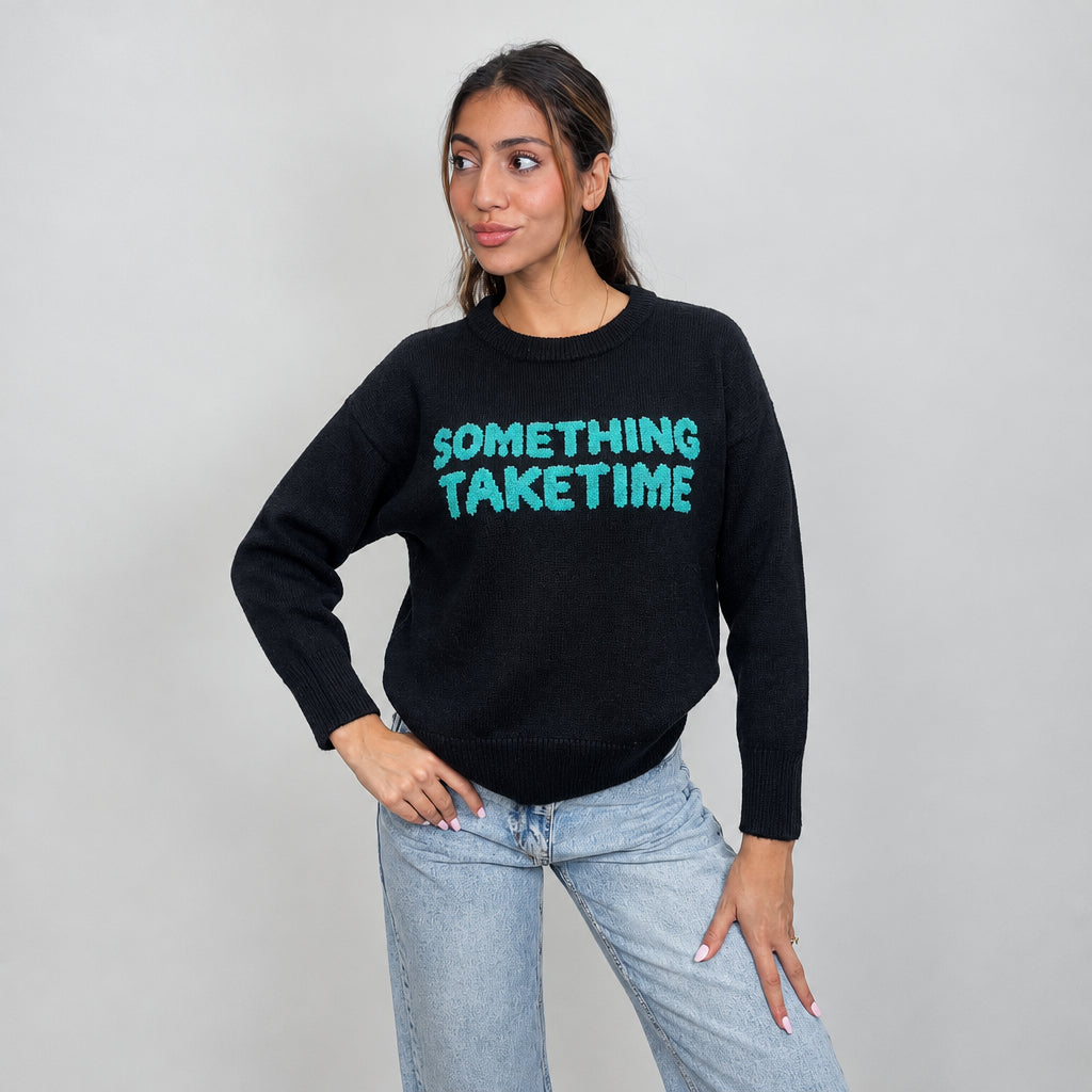Black slogan sweater with ribbed cuffs, worn with light wash jeans