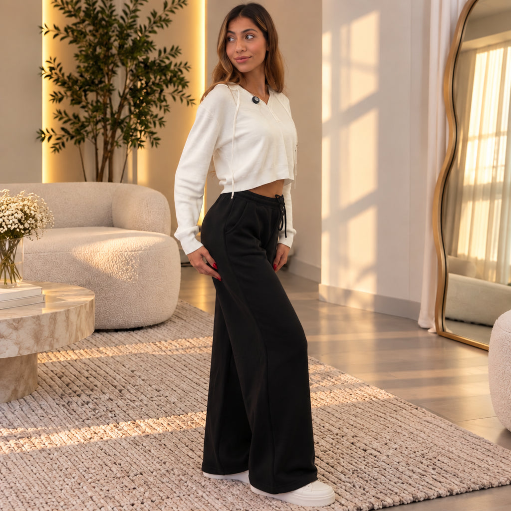 Side view of black wide leg sweatpants with a relaxed straight fall, worn with white trainers