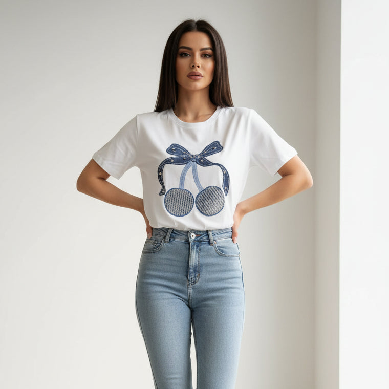 Woman wearing a white tshirt with a blue cherry design and light blue jeans on a plain background