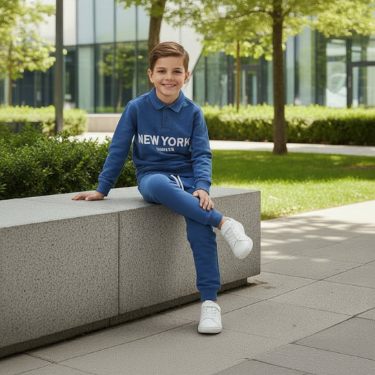 Boy seated outdoors in a blue long sleeve New York top and blue joggers, two piece set