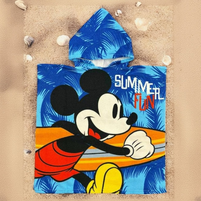 Blue Mickey Mouse poncho towel with palm leaves and a surfboard print flat lay on sand