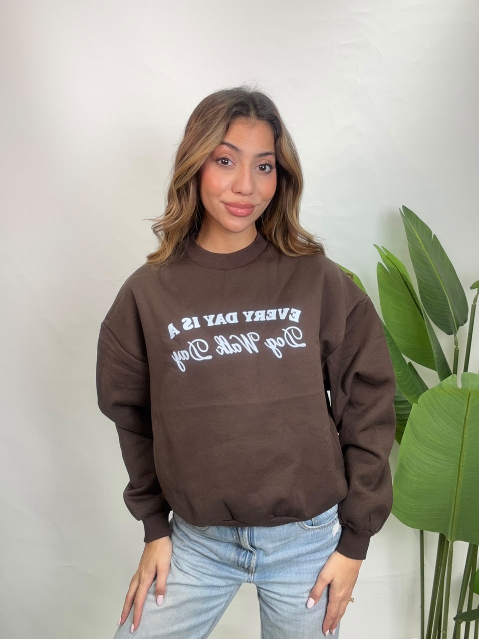 Woman in a brown crew neck sweatshirt with an Every Day Is A Dog Walk Day slogan and light jeans
