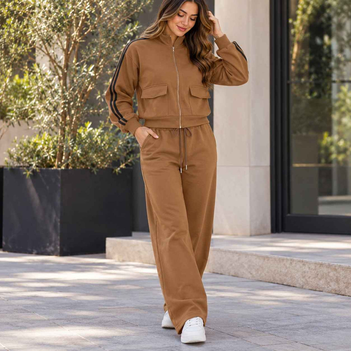 Woman in a camel zip jacket with black sleeve stripes and matching wide leg pants by a planter