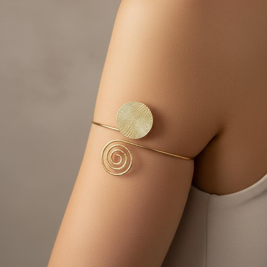 Gold arm cuffs on a person's arm against a neutral background