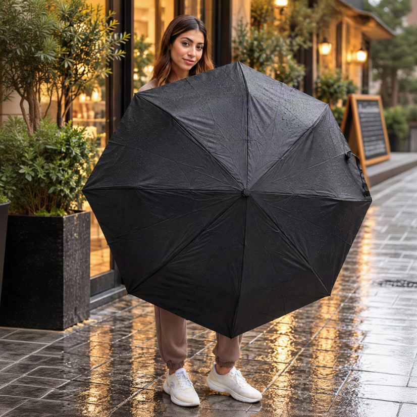 Woman holding open a plain black folding umbrella beaded with raindrops