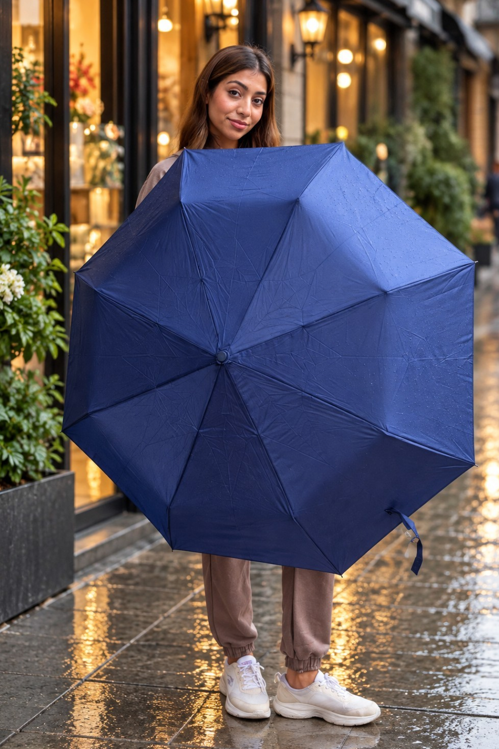 Woman holding open a plain navy folding umbrella outside a lit shopfront