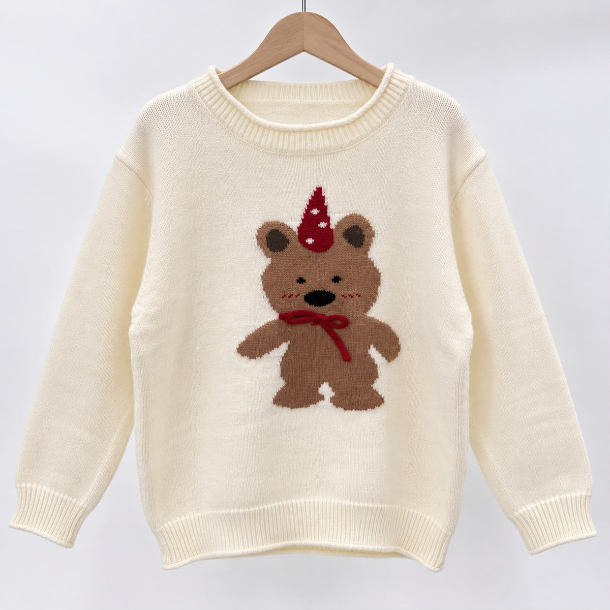 Cream knit sweater on a hanger with a brown teddy bear wearing a red party hat