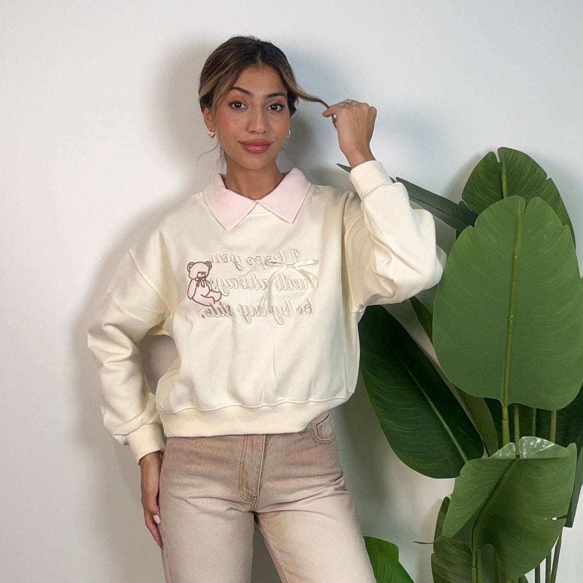 Cream teddy bear sweatshirt worn with beige jeans against a plain wall