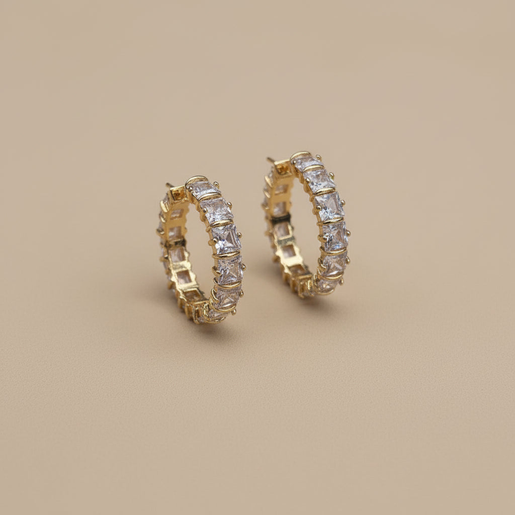 Gold crystal hoop earrings on a beige background