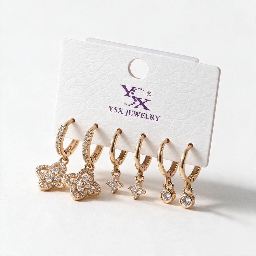 Three pairs of gold huggies with crystal quatrefoil, star and round bezel drops on a white card