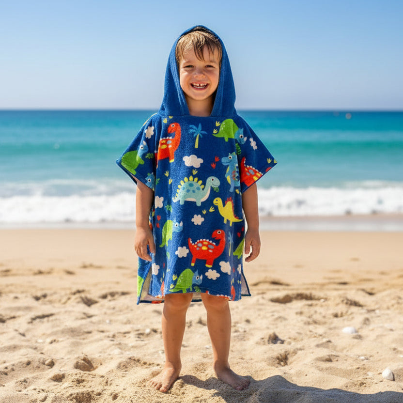 Boy on the beach in a royal blue poncho towel covered in small colourful dinosaurs