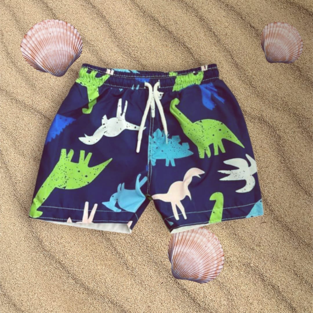 Navy blue swim shorts with dinosaur patterns on sand with shells