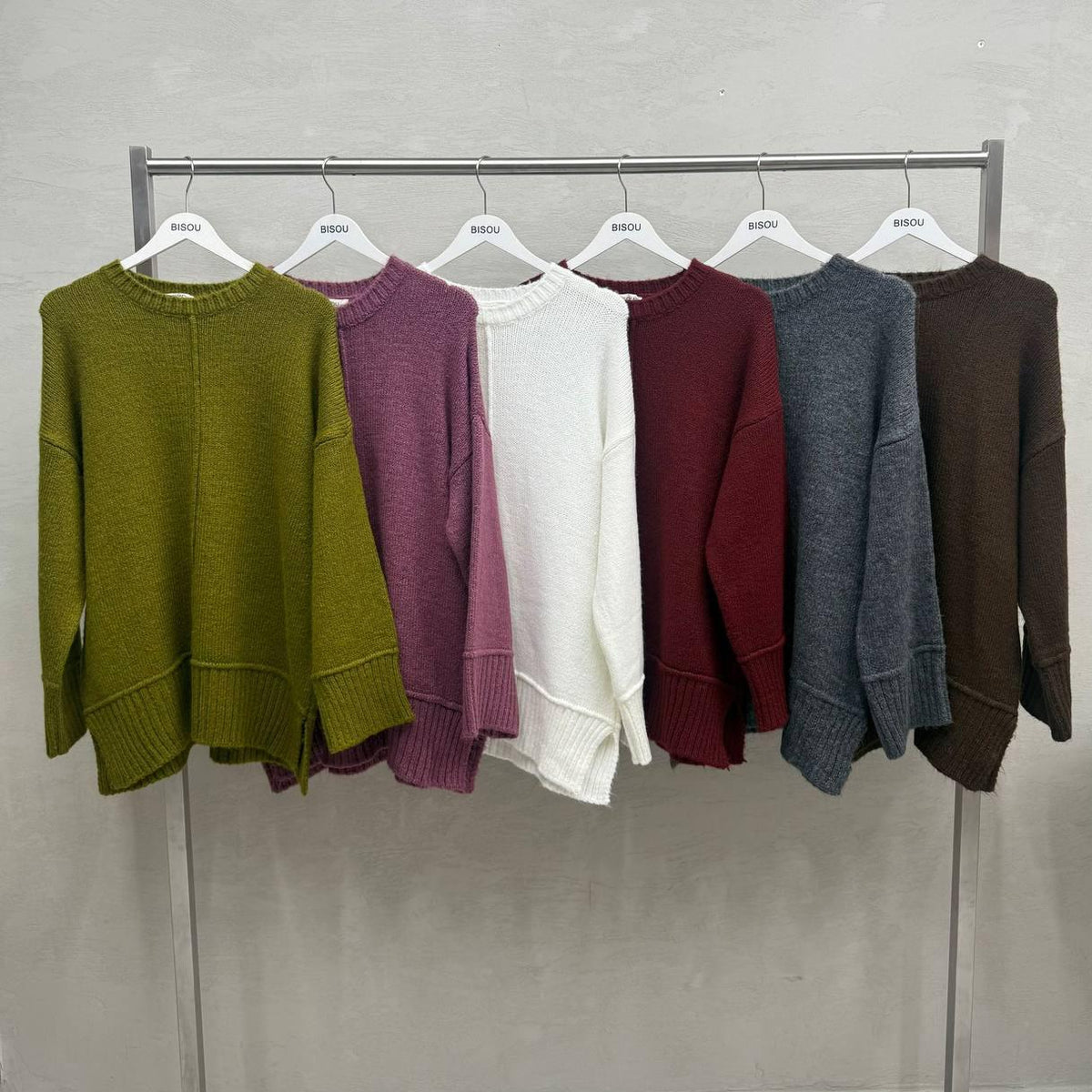 Six drop shoulder knit tops hanging on a rail, side slits visible at the hem