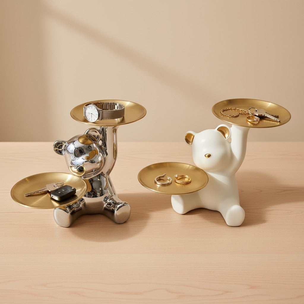 Two bear-shaped jewelry stands, one silver and one white, holding keys and rings on a wooden surface.