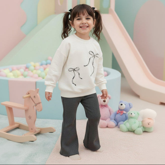Girl in a cream bow print sweatshirt and charcoal flared pants