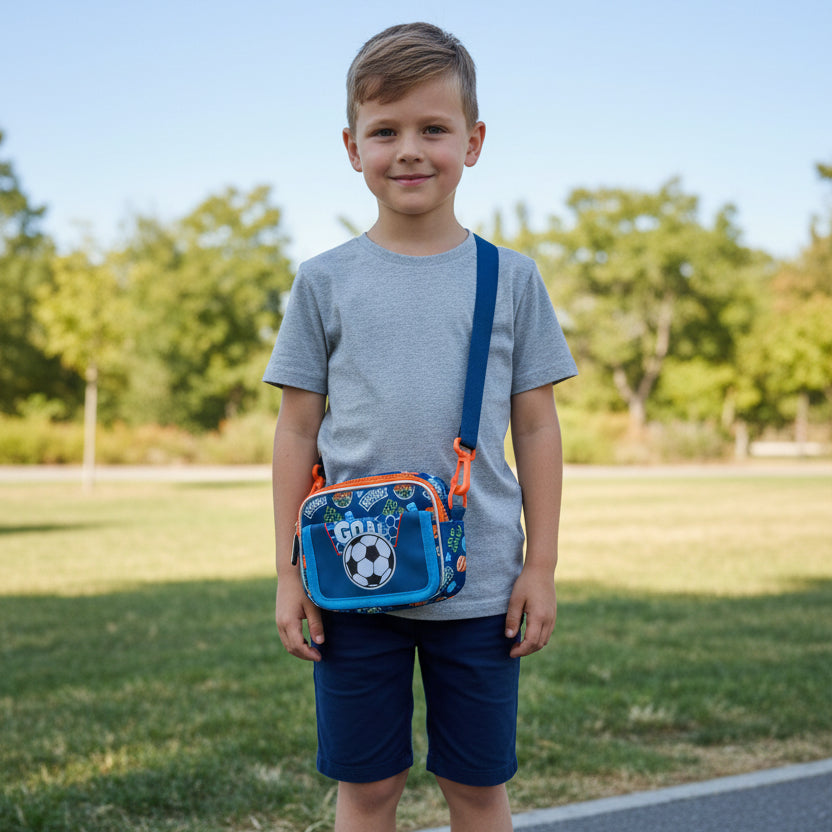 Boy wearing a blue football themed cross body bag with orange trim outdoors in a park