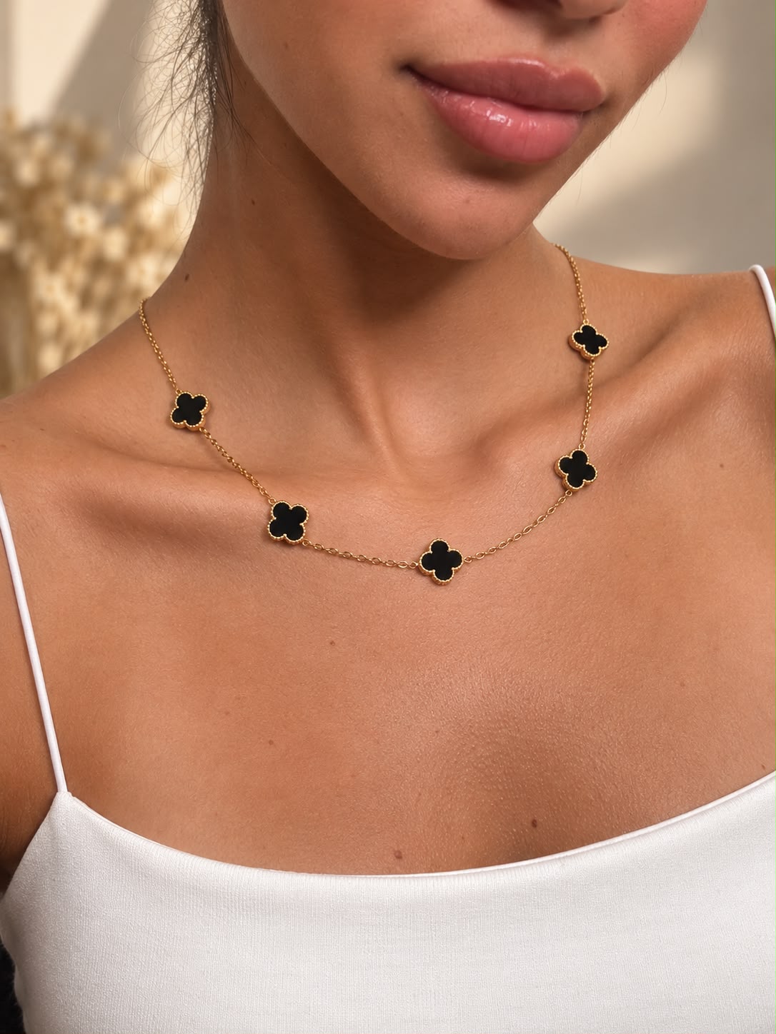 Gold tone necklace with five black clover charms worn at the collarbone with a white cami
