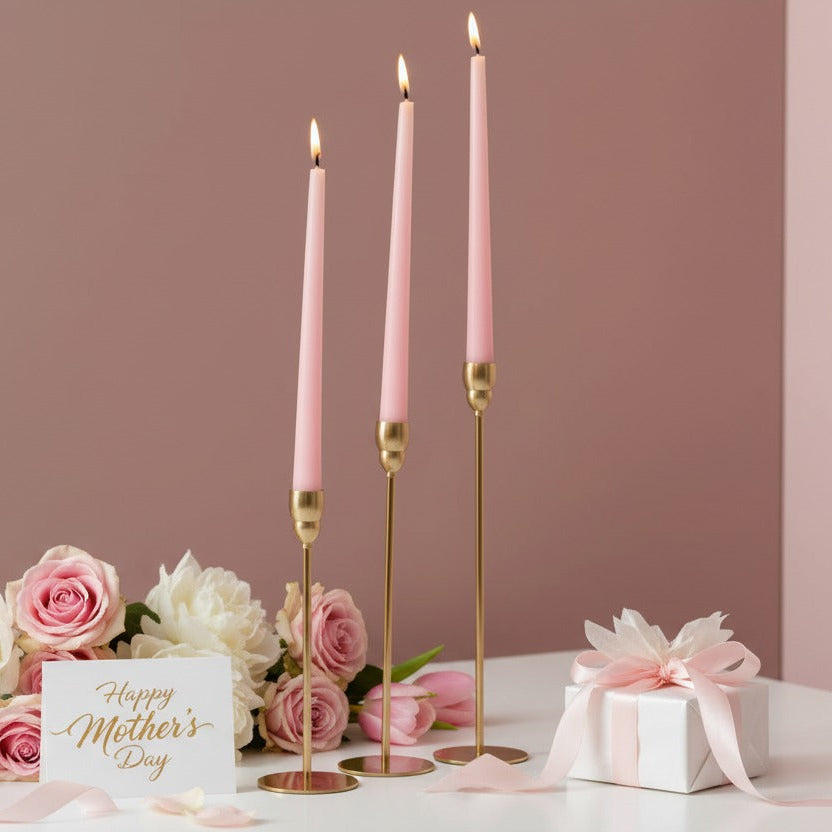 Three lit pink tapers on slim gold rods among roses, tulips and a ribboned box