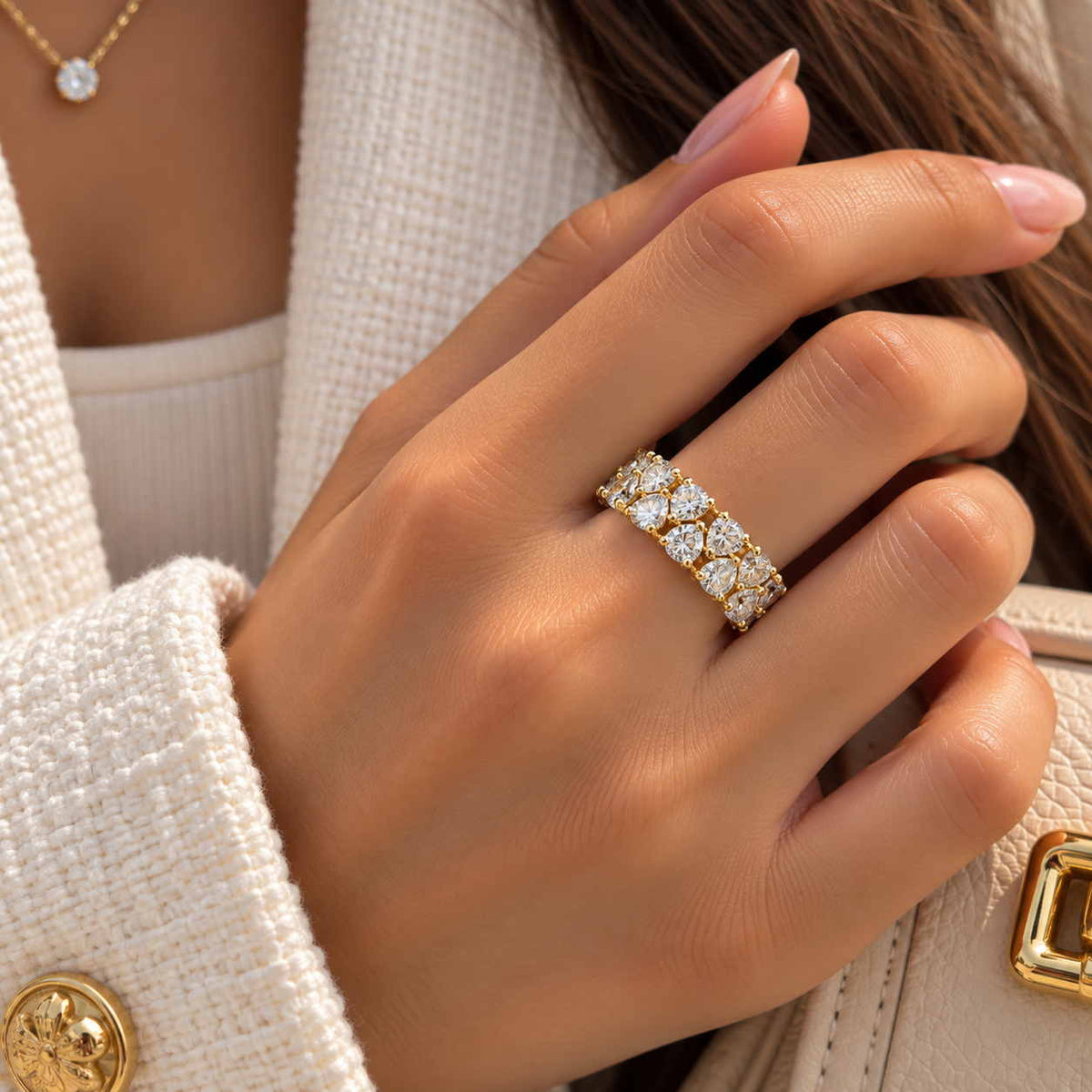 Hand wearing a wide gold ring with two rows of large round crystals against a cream tweed jacket