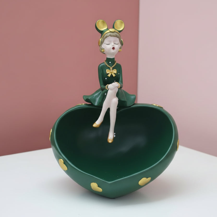 Dark green heart bowl studded with gold hearts, a girl in a green dress seated on the rim