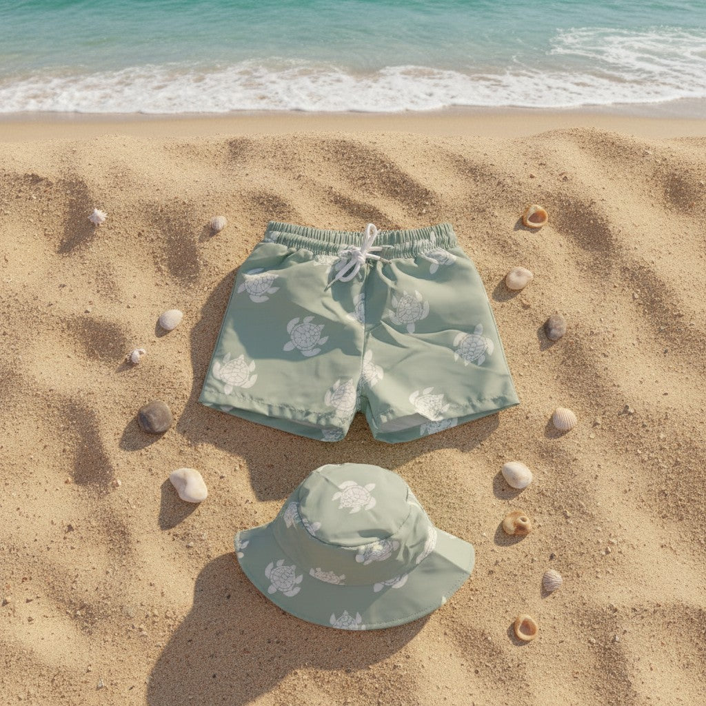 A pair of sage green swim trunks and a matching sun hat with a white sea turtle pattern