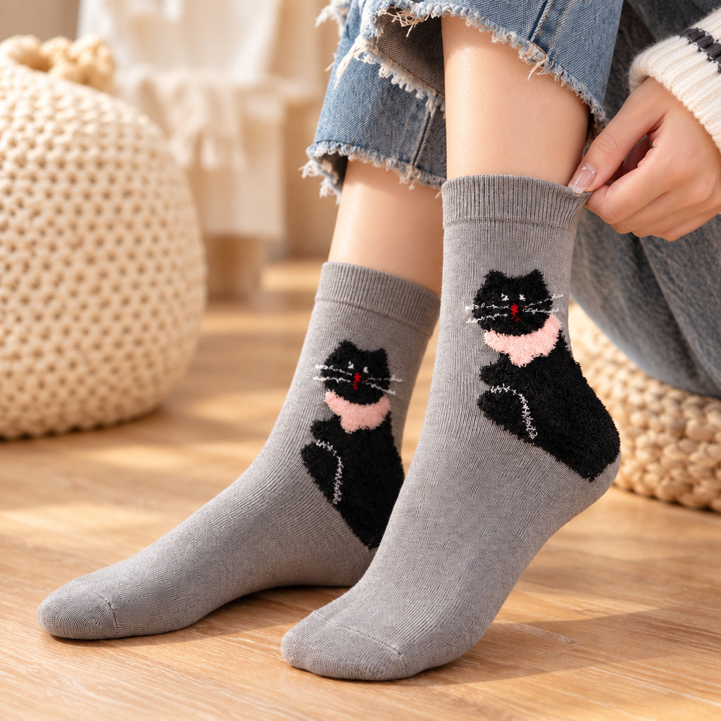 Woman in jeans wearing grey crew socks with a fuzzy black cat in a pink scarf on a wooden floor