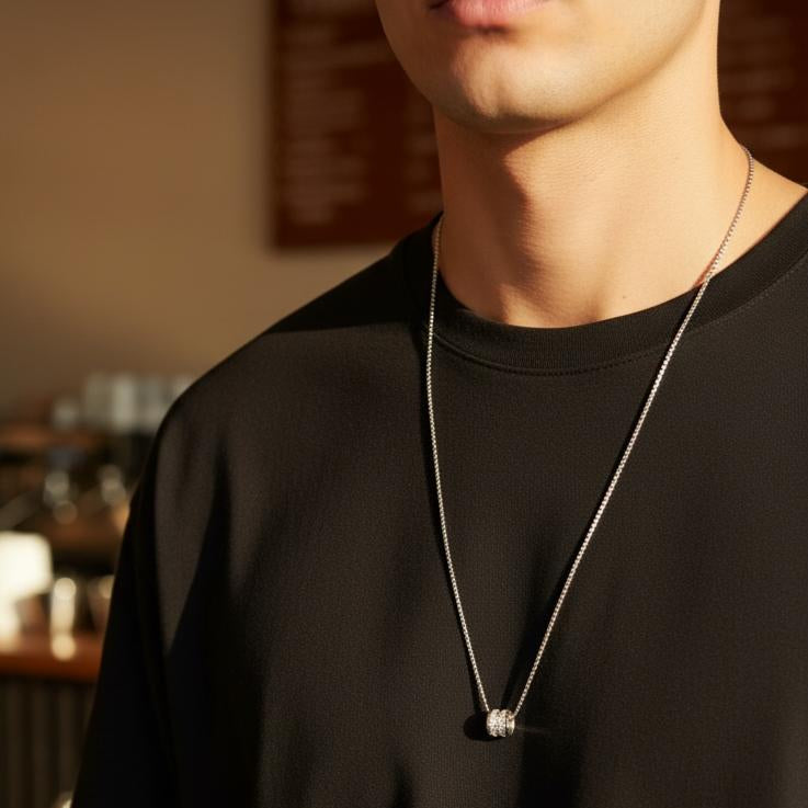 Halo cylinder pendant necklace worn over a black tee in a warm cafe