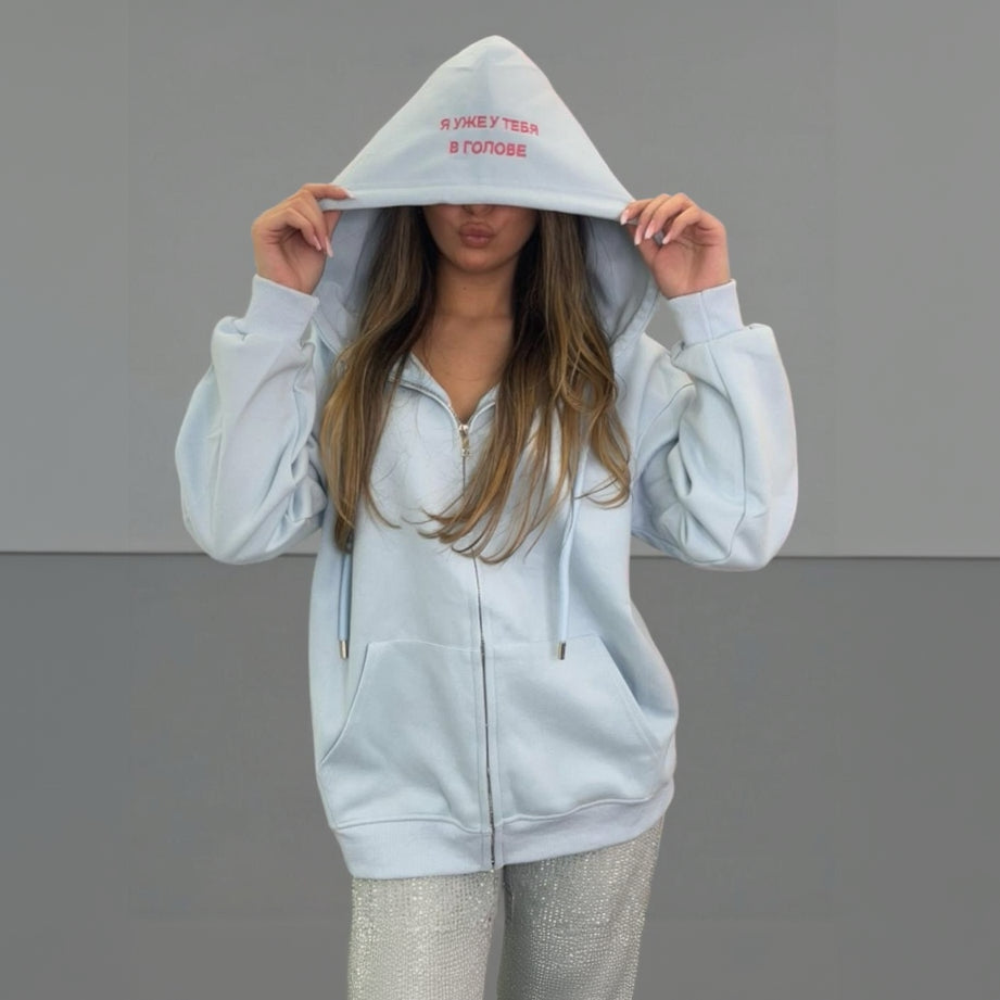 Person wearing a light grey zip jacket with text on the hood against a plain background