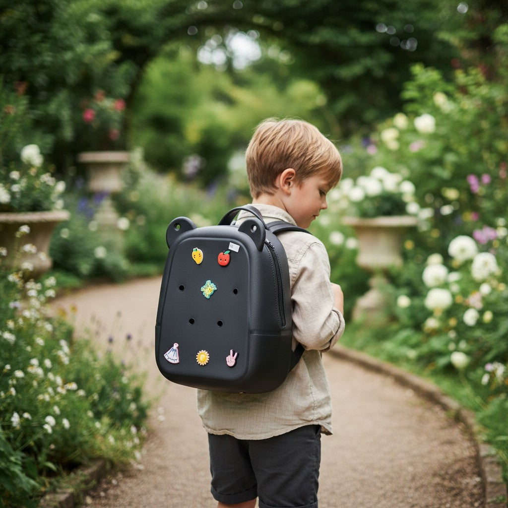Boy wearing a black hard shell backpack with bear ears and colourful fruit, flower and peace sign charms