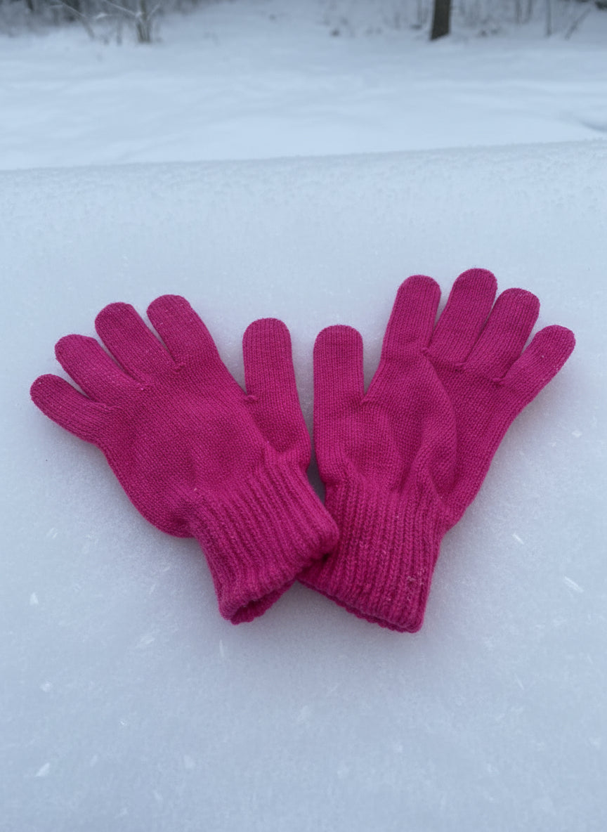 Hot pink knitted gloves laid side by side on snow