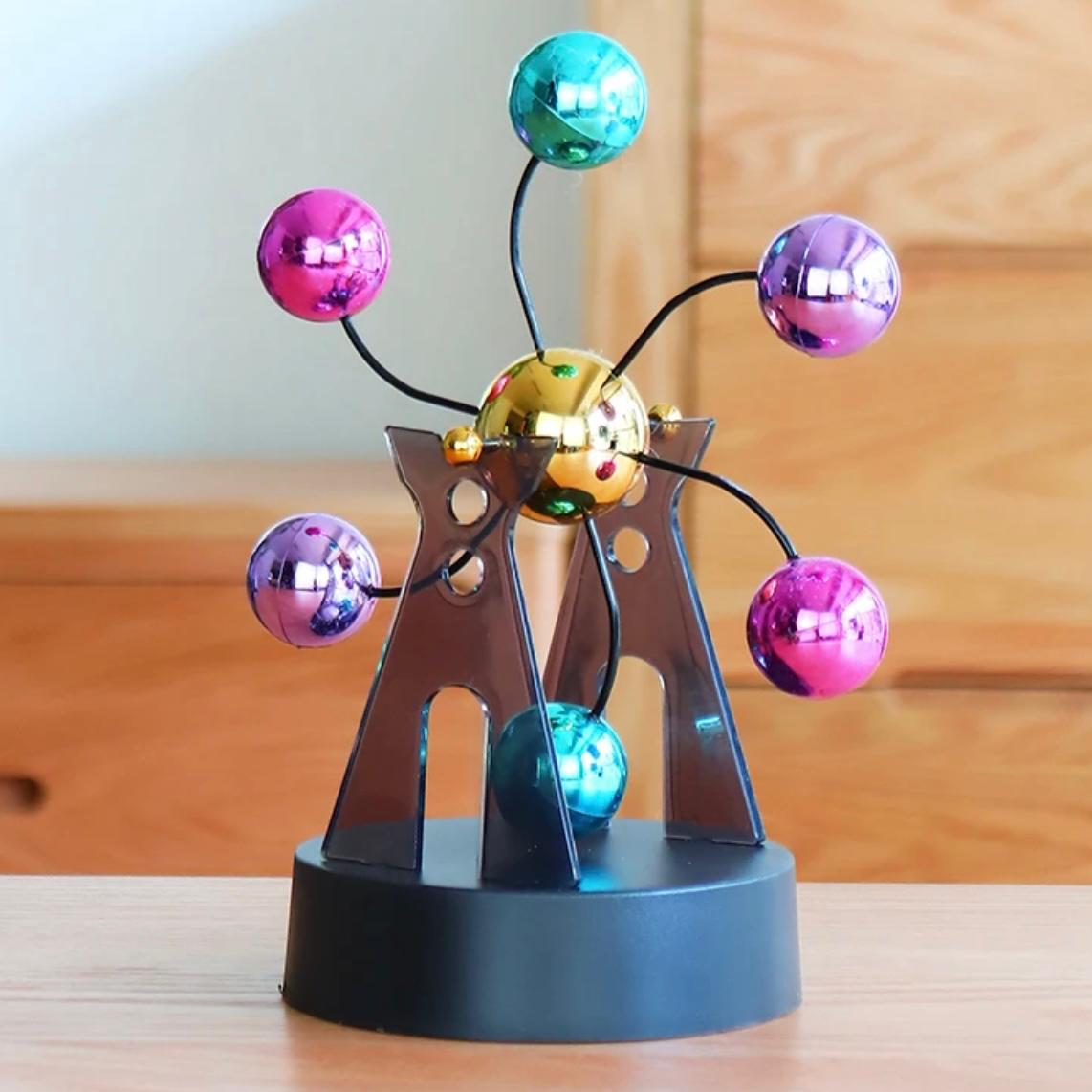Kinetic desk gadget standing on a wooden desk with six coloured chrome balls