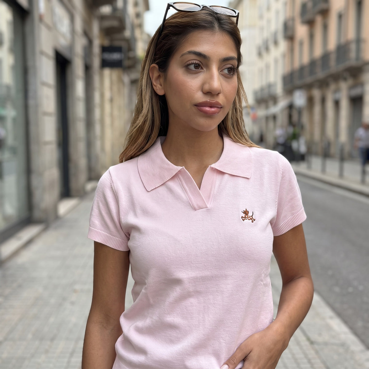 Pale pink knit polo top with an open neckline and tan embroidered motif