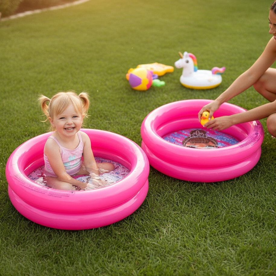 Bright pink inflatable ring pools on grass with a toddler splashing in shallow water