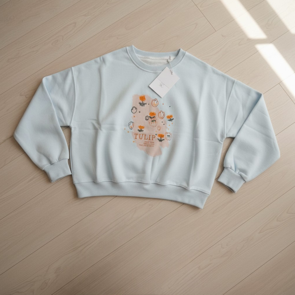Light blue tulip print sweatshirt laid flat on a pale wood floor with its tag