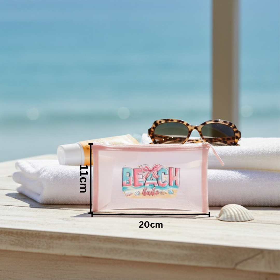 Pink pouch with 'BEACH babe' text on a wooden surface with towels and sunglasses, beach setting.
