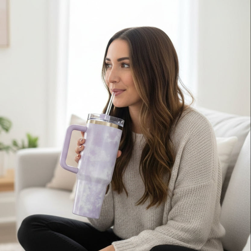 Lilac tie dye marble tumbler with a clear lid and straw held on a white sofa