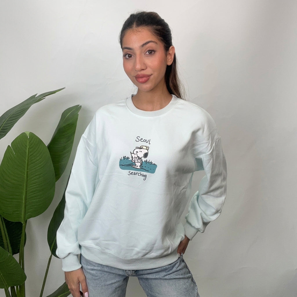 Woman wearing a mint crew neck sweatshirt with a puppy scout graphic, styled with light wash jeans