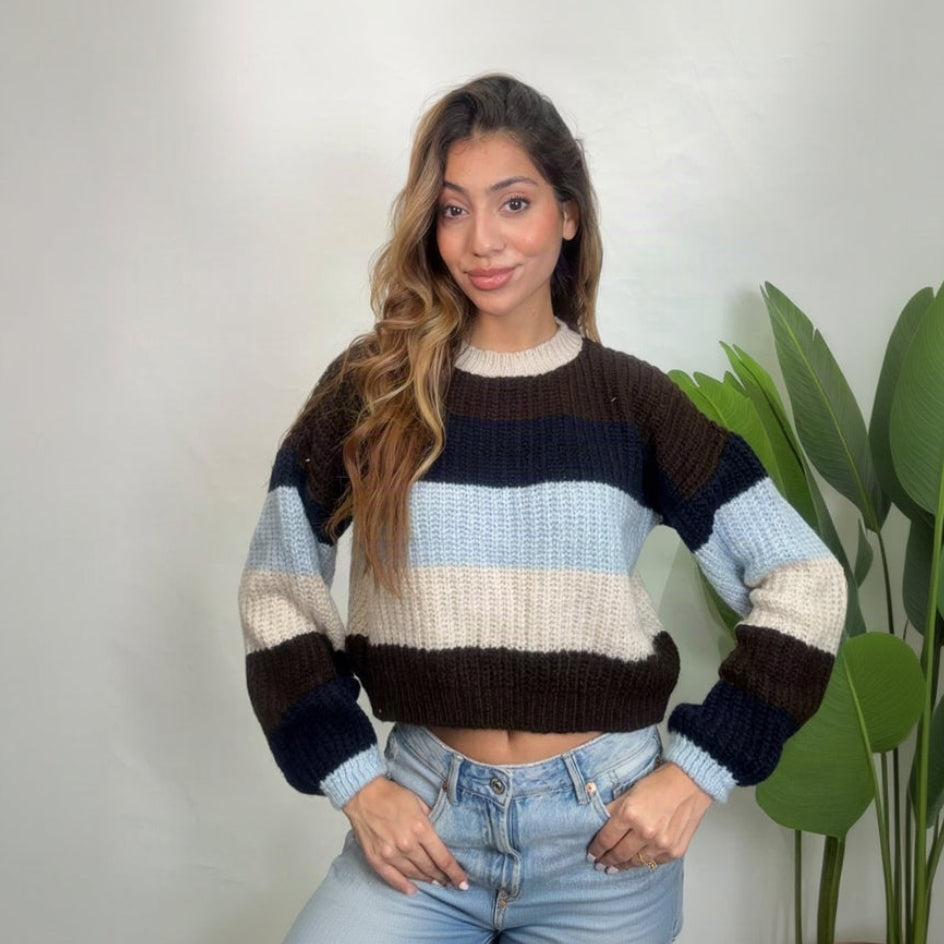 Woman in a navy, brown, light blue and cream striped sweater with hands in her jeans pockets