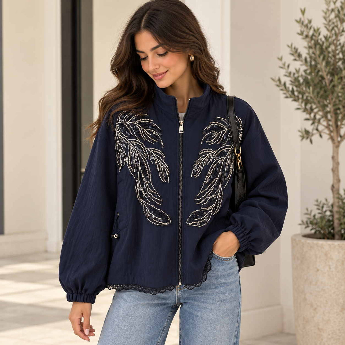 Woman in a navy zip jacket with silver beaded leaf sprays, balloon sleeves and a lace trimmed hem